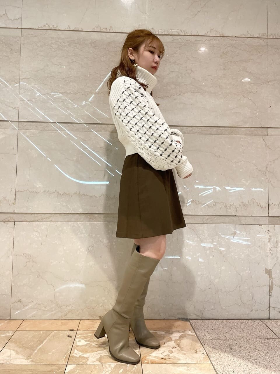 ブラウン系のスカート、ベージュ系のブーツ、ホワイト系のニット/セーターを着用したレディースの秋コーディネートの2枚目の写真