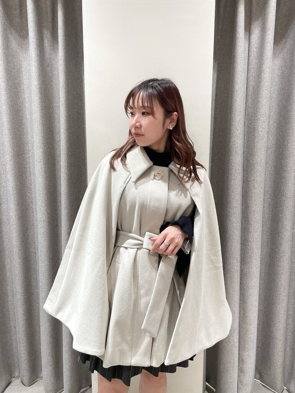 ホワイト系のポンチョ、ブラック系のニット/セーター、グレー系のスカートを着用したレディースの冬コーディネートの6枚目の写真