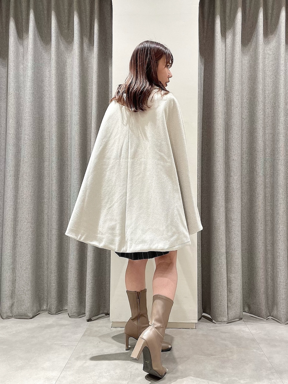 ホワイト系のポンチョ、ブラック系のニット/セーター、グレー系のスカートを着用したレディースの冬コーディネートの3枚目の写真