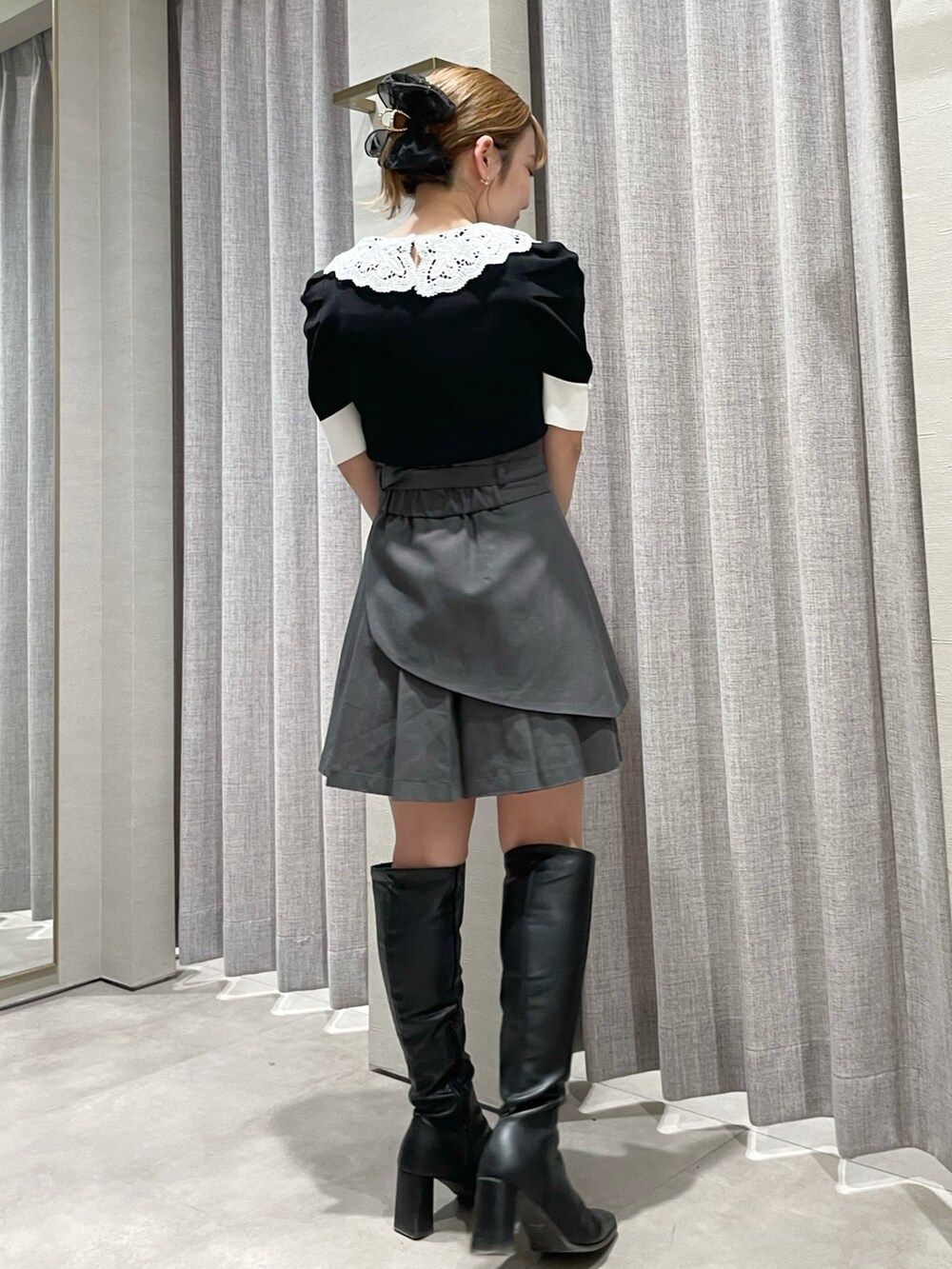 ブラック系のニット/セーター、グレー系のスカート、ブラック系のブーツを着用したレディースの春コーディネートの2枚目の写真