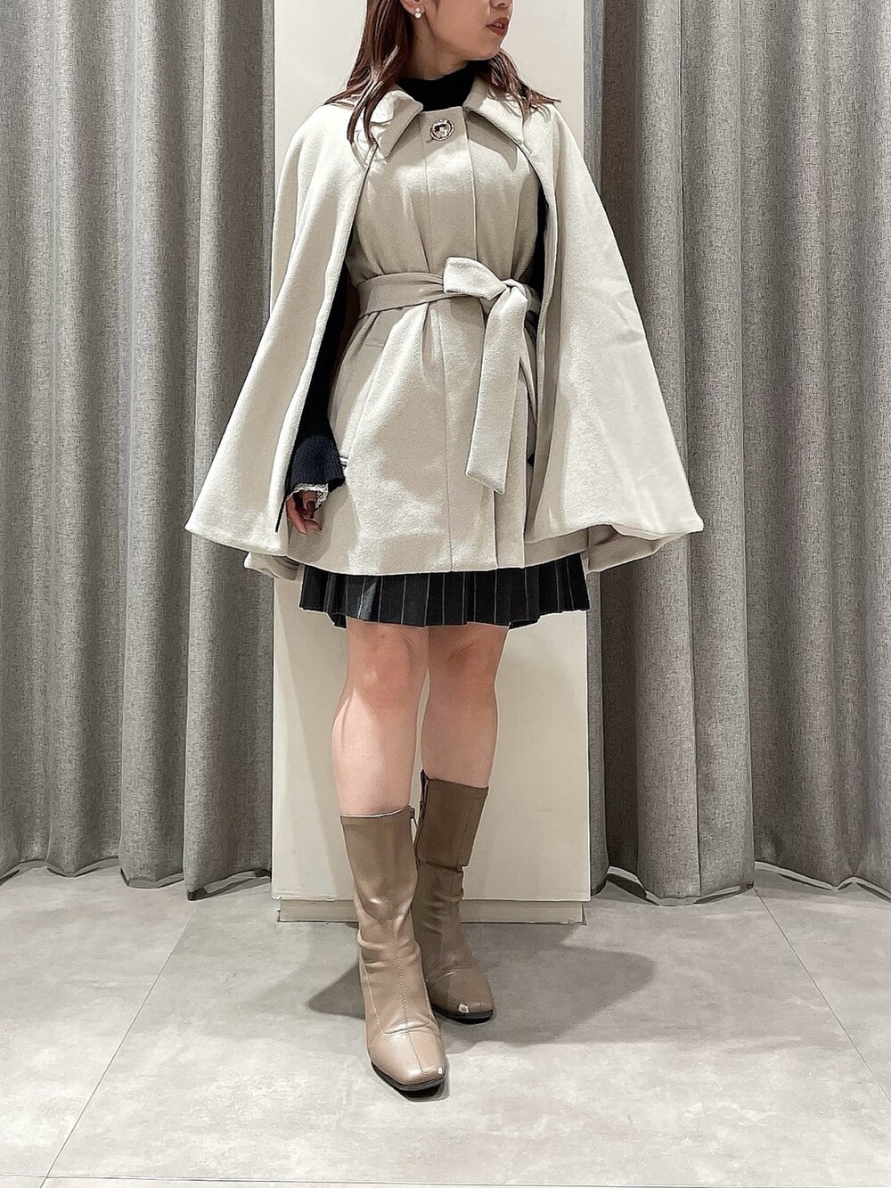 ホワイト系のポンチョ、ブラック系のニット/セーター、グレー系のスカートを着用したレディースの冬コーディネートの5枚目の写真