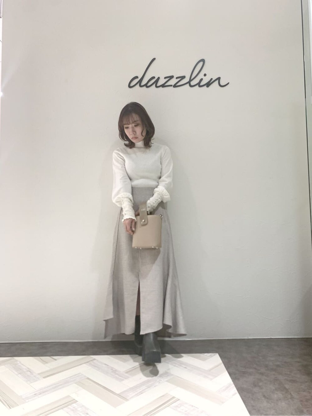 グレー系のブーツ、グレー系のスカート、ベージュ系のハンドバッグを着用したレディースの秋コーディネートの4枚目の写真