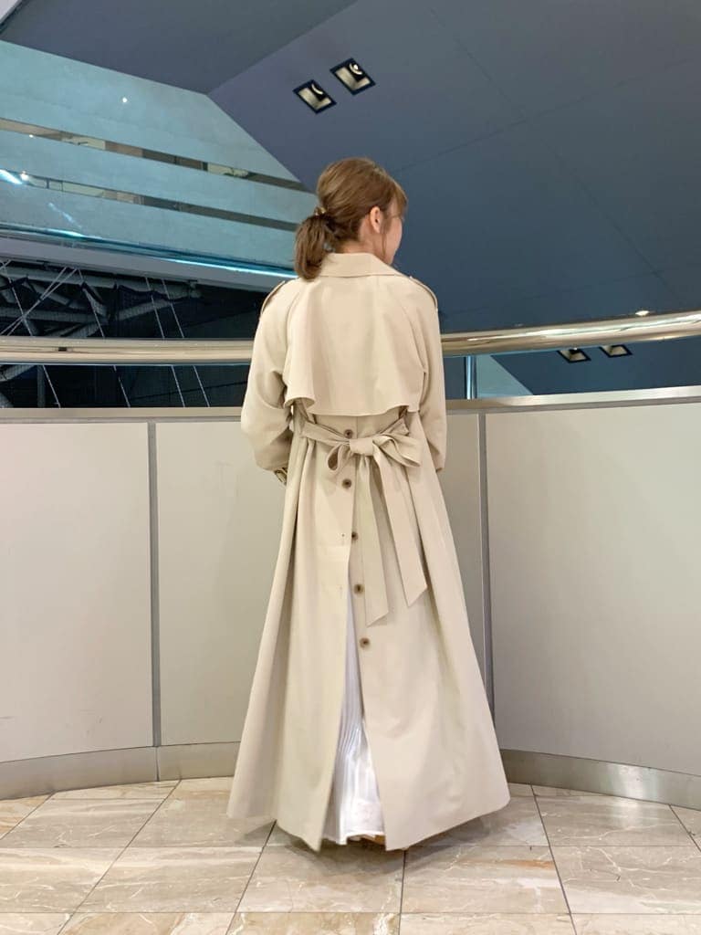 ベージュ系のトレンチコート、オレンジ系のワンピース、ホワイト系のパンプスを着用したレディースの冬コーディネートの7枚目の写真