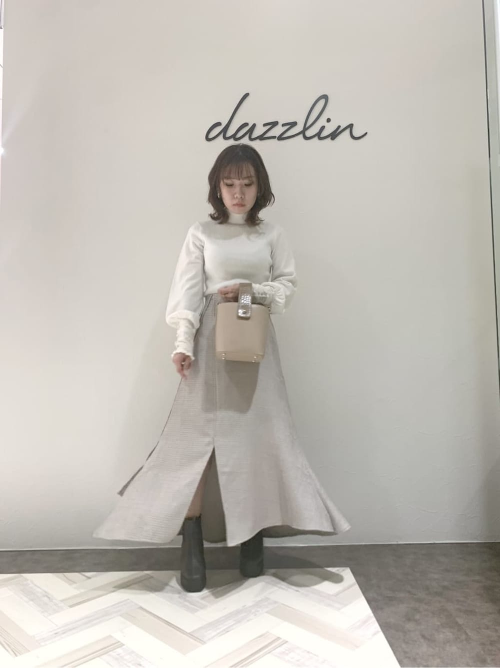 グレー系のブーツ、グレー系のスカート、ベージュ系のハンドバッグを着用したレディースの秋コーディネートの6枚目の写真