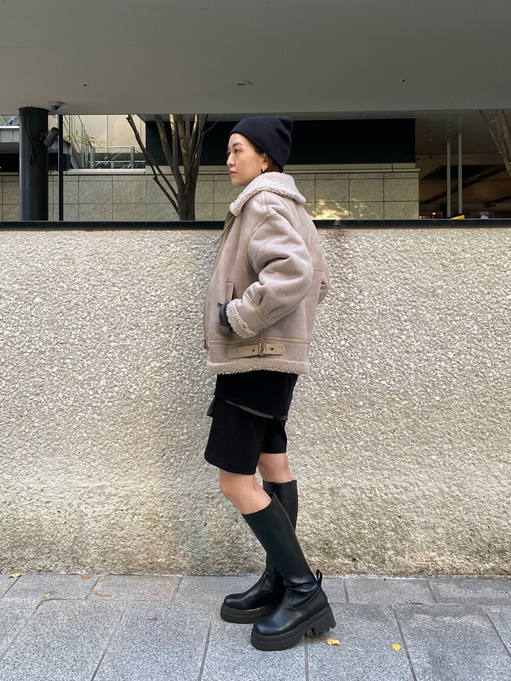 ベージュ系のムートンコート、ブラック系のニット/セーター、ブラック系のブーツを着用したレディースの秋コーディネートの2枚目の写真