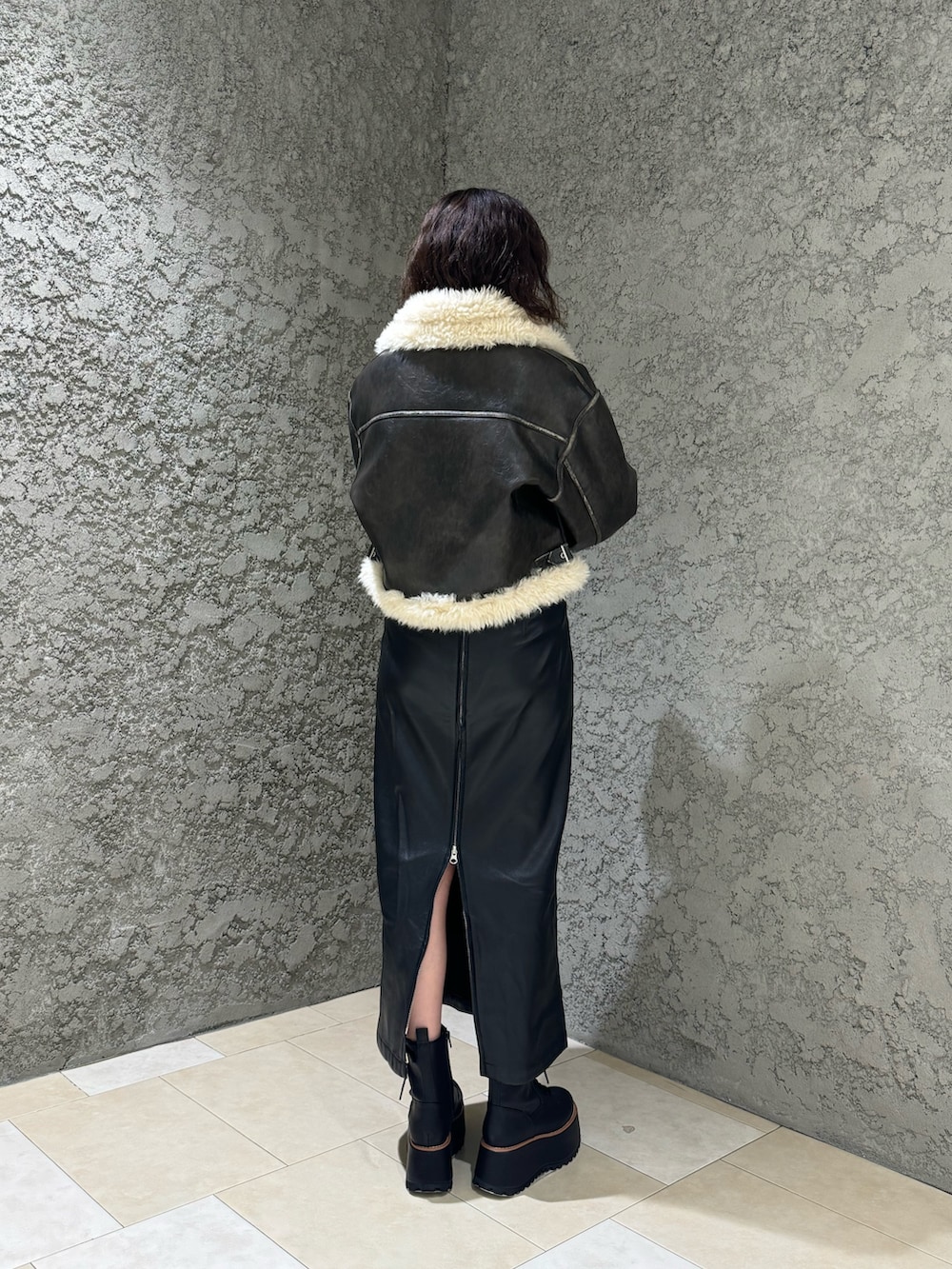 ブラック系のスカート、ブラック系のブーツ、ブラウン系のムートンコートを着用したレディースの夏コーディネートの3枚目の写真