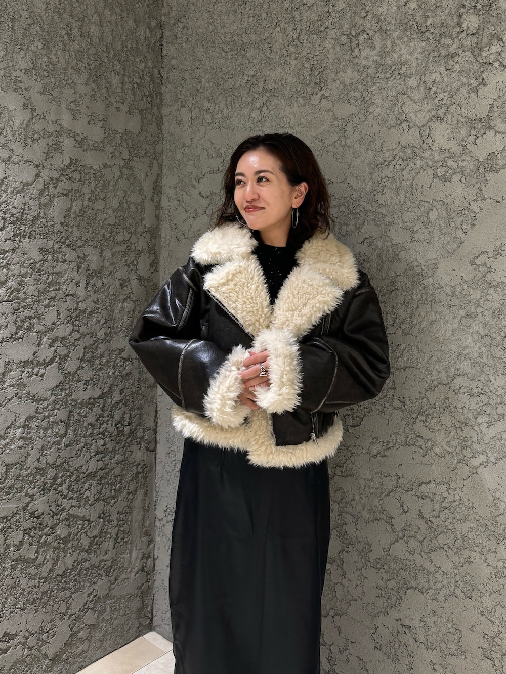 ブラック系のスカート、ブラック系のブーツ、ブラウン系のムートンコートを着用したレディースの夏コーディネートの6枚目の写真