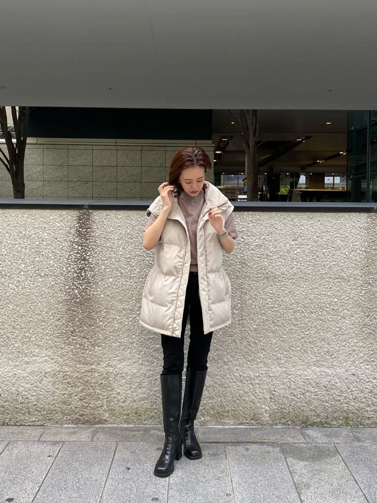 ブラック系のデニムパンツ、ベージュ系のニット/セーター、ホワイト系のダウンベストを着用したレディースの秋コーディネートの3枚目の写真