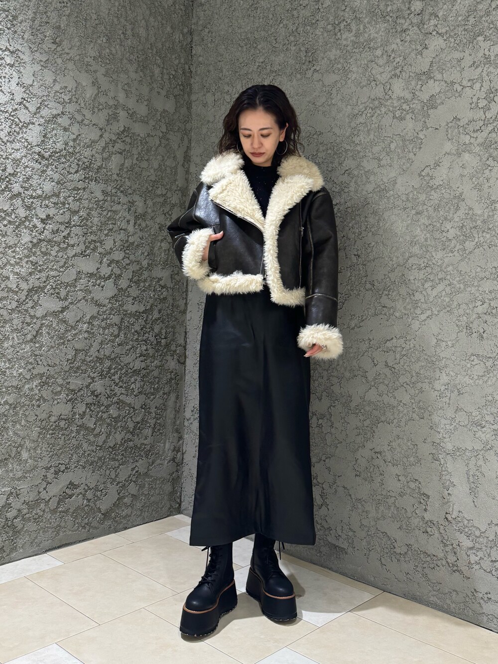 ブラック系のスカート、ブラック系のブーツ、ブラウン系のムートンコートを着用したレディースの夏コーディネートの2枚目の写真