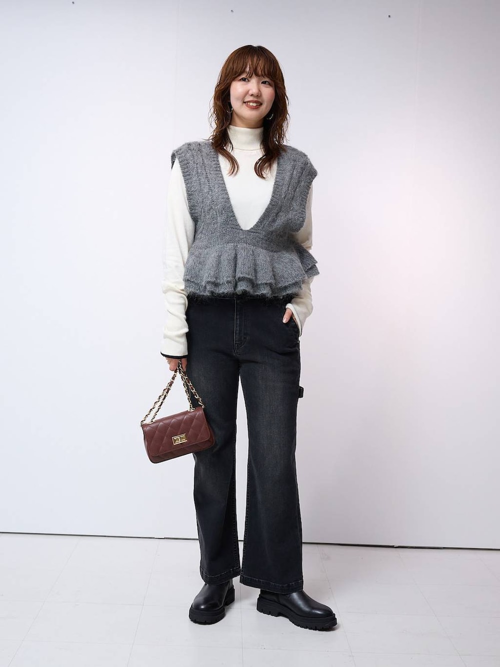 ブラウン系のハンドバッグ、ホワイト系のニット/セーター、グレー系のベストを着用したレディースの秋コーディネートの2枚目の写真