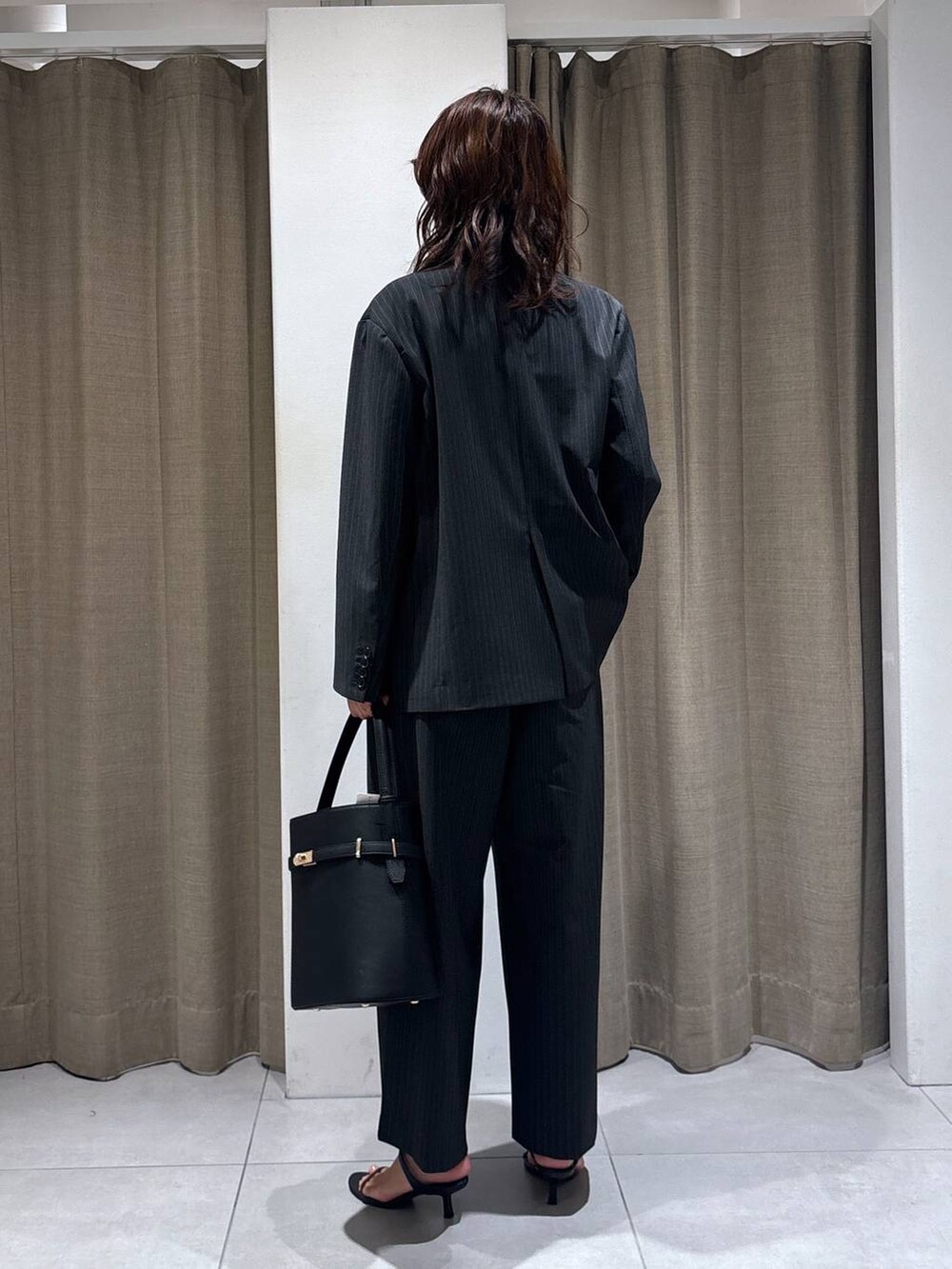 グレー系のスラックス、グレー系のテーラードジャケット、ブラック系のハンドバッグを着用したレディースの秋コーディネートの3枚目の写真