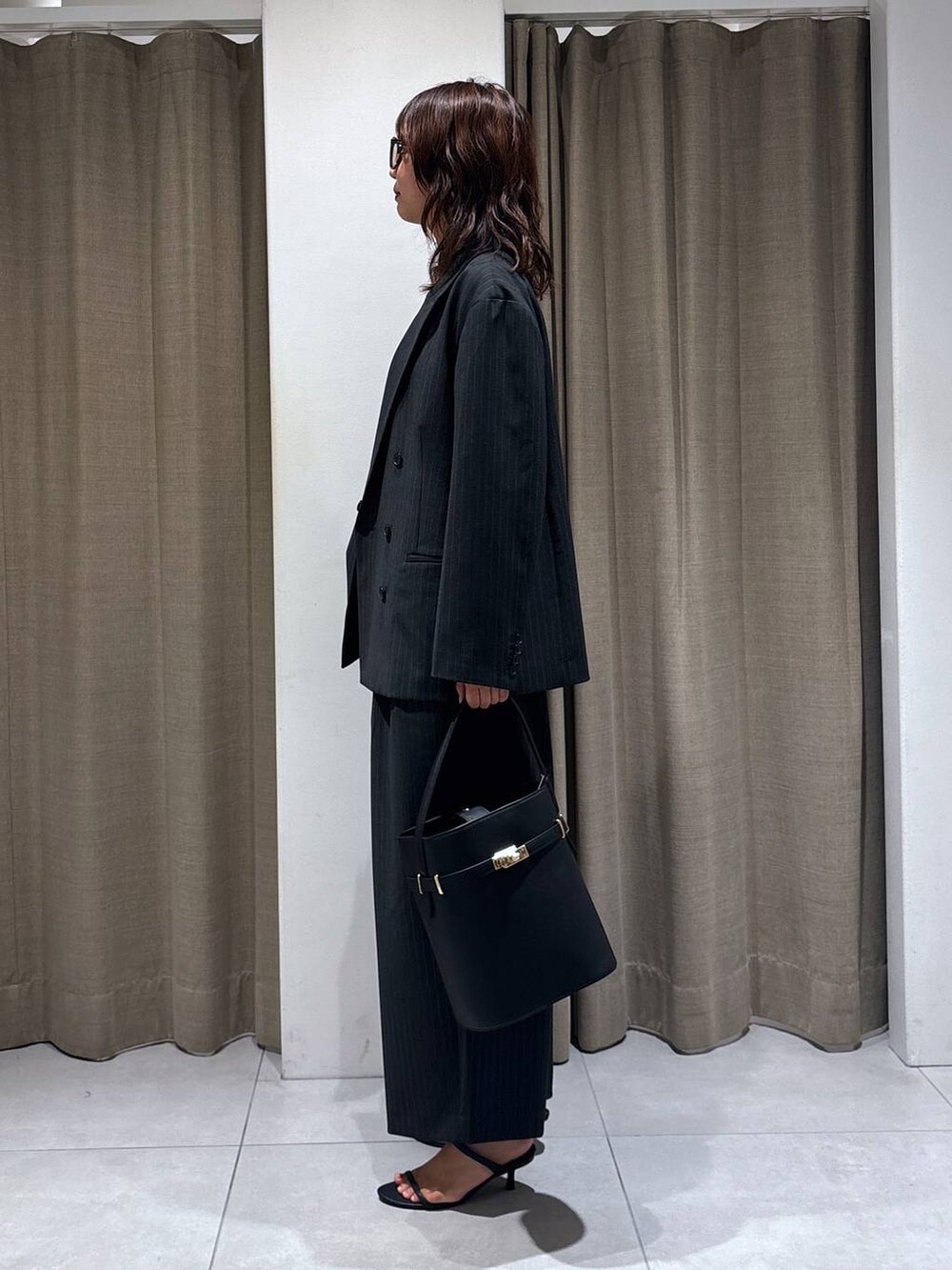 グレー系のスラックス、グレー系のテーラードジャケット、ブラック系のハンドバッグを着用したレディースの秋コーディネートの2枚目の写真