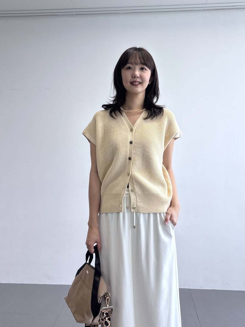 イエロー系のトートバッグ、ホワイト系のベスト、ホワイト系のスニーカーを着用したレディースの冬コーディネートの2枚目の写真