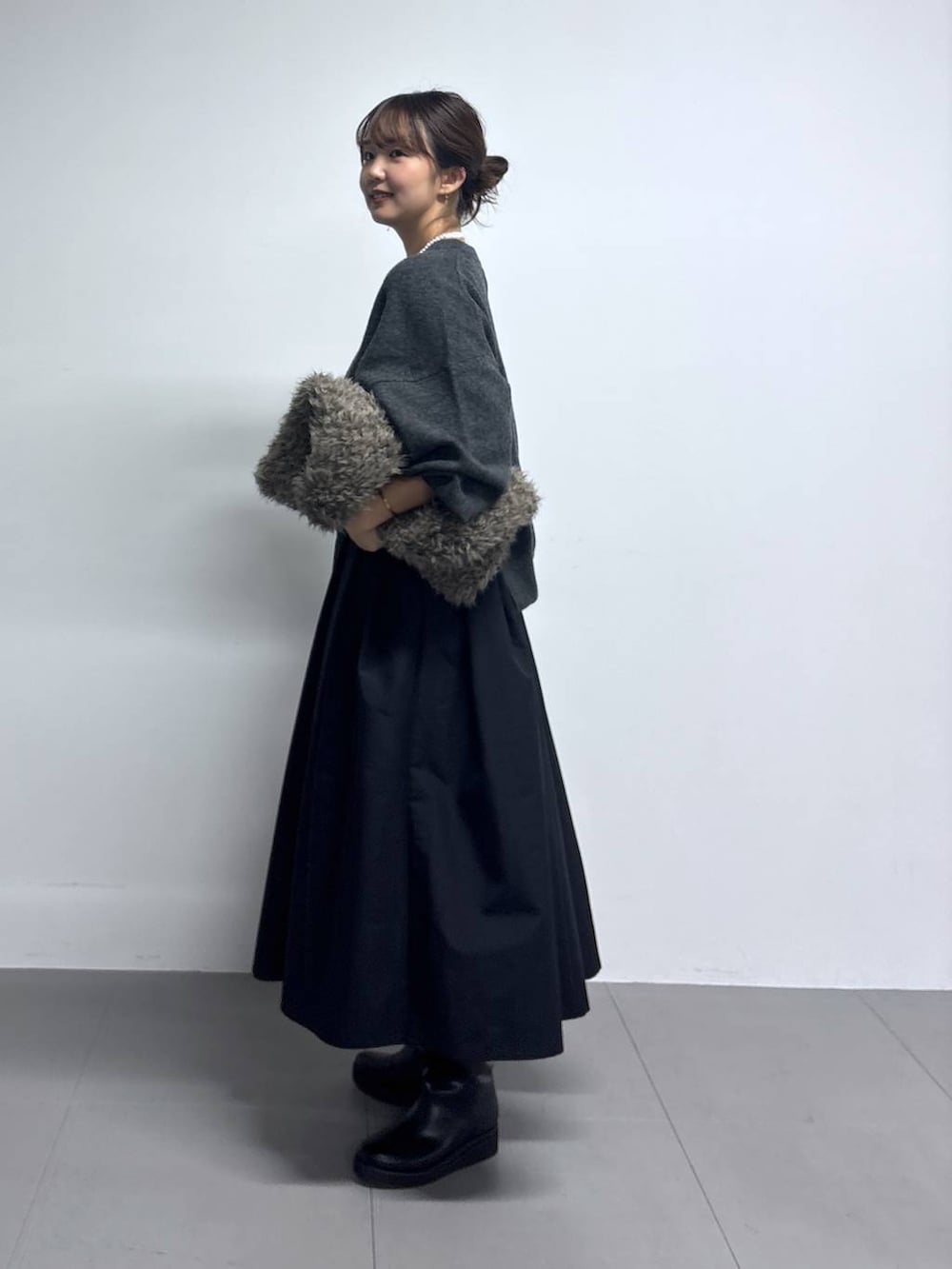 グレー系のニット/セーター、ブラウン系のハンドバッグ、ブラック系のブーツを着用したレディースの秋コーディネートの2枚目の写真