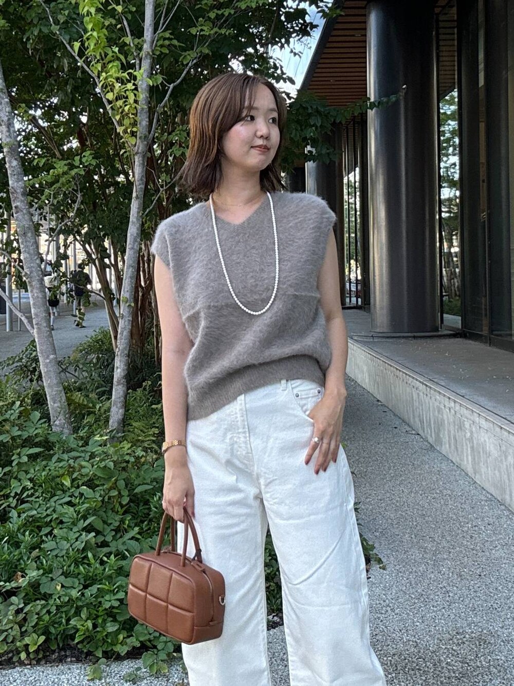 ブラック系のスリッポン、ブラウン系のハンドバッグ、ホワイト系のデニムパンツを着用したレディースの夏コーディネートの2枚目の写真