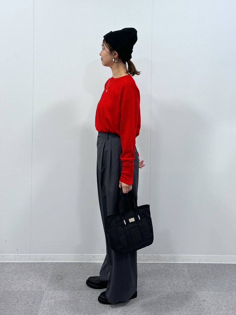 グレー系のスラックス、ブラック系のトートバッグ、レッド系のニット/セーターを着用したレディースの秋コーディネートの3枚目の写真