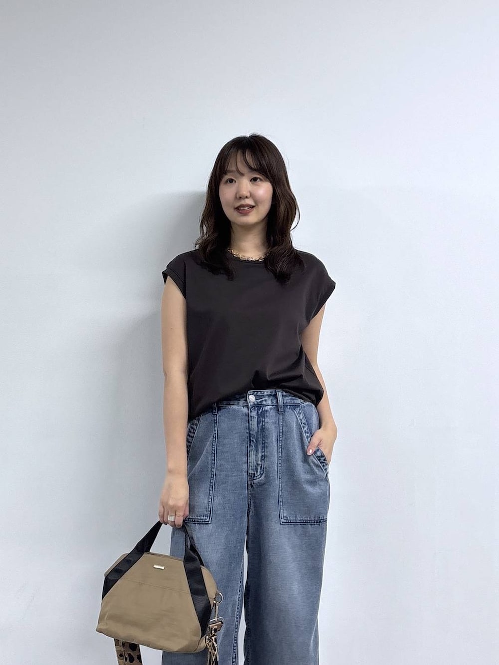 イエロー系のトートバッグ、ブラウン系のTシャツ/カットソー、ブルー系のデニムパンツを着用したレディースの春コーディネートの2枚目の写真