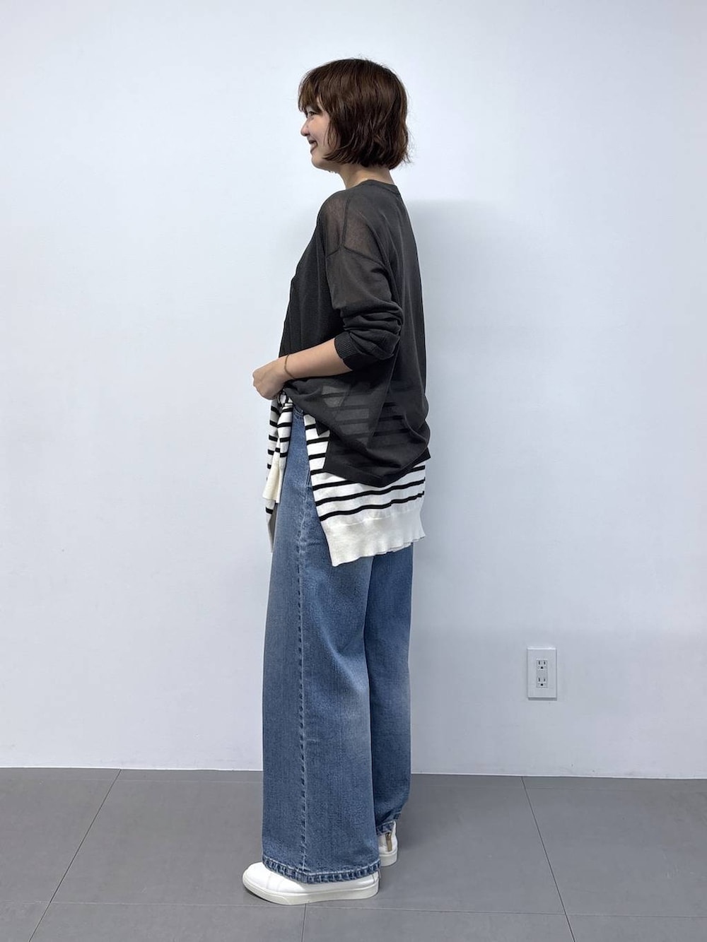 グレー系のニット/セーター、ブラック系のショルダーバッグ、ブルー系のデニムパンツを着用したレディースの秋コーディネートの3枚目の写真