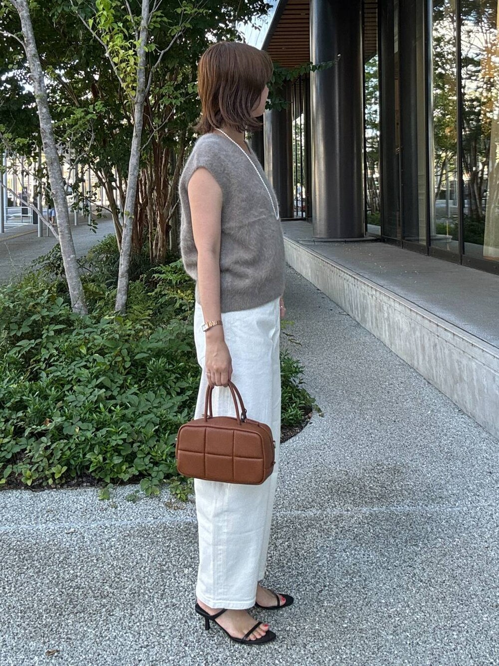 ブラック系のスリッポン、ブラウン系のハンドバッグ、ホワイト系のデニムパンツを着用したレディースの夏コーディネートの3枚目の写真