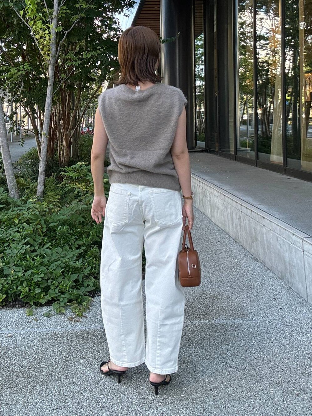 ブラック系のスリッポン、ブラウン系のハンドバッグ、ホワイト系のデニムパンツを着用したレディースの夏コーディネートの5枚目の写真