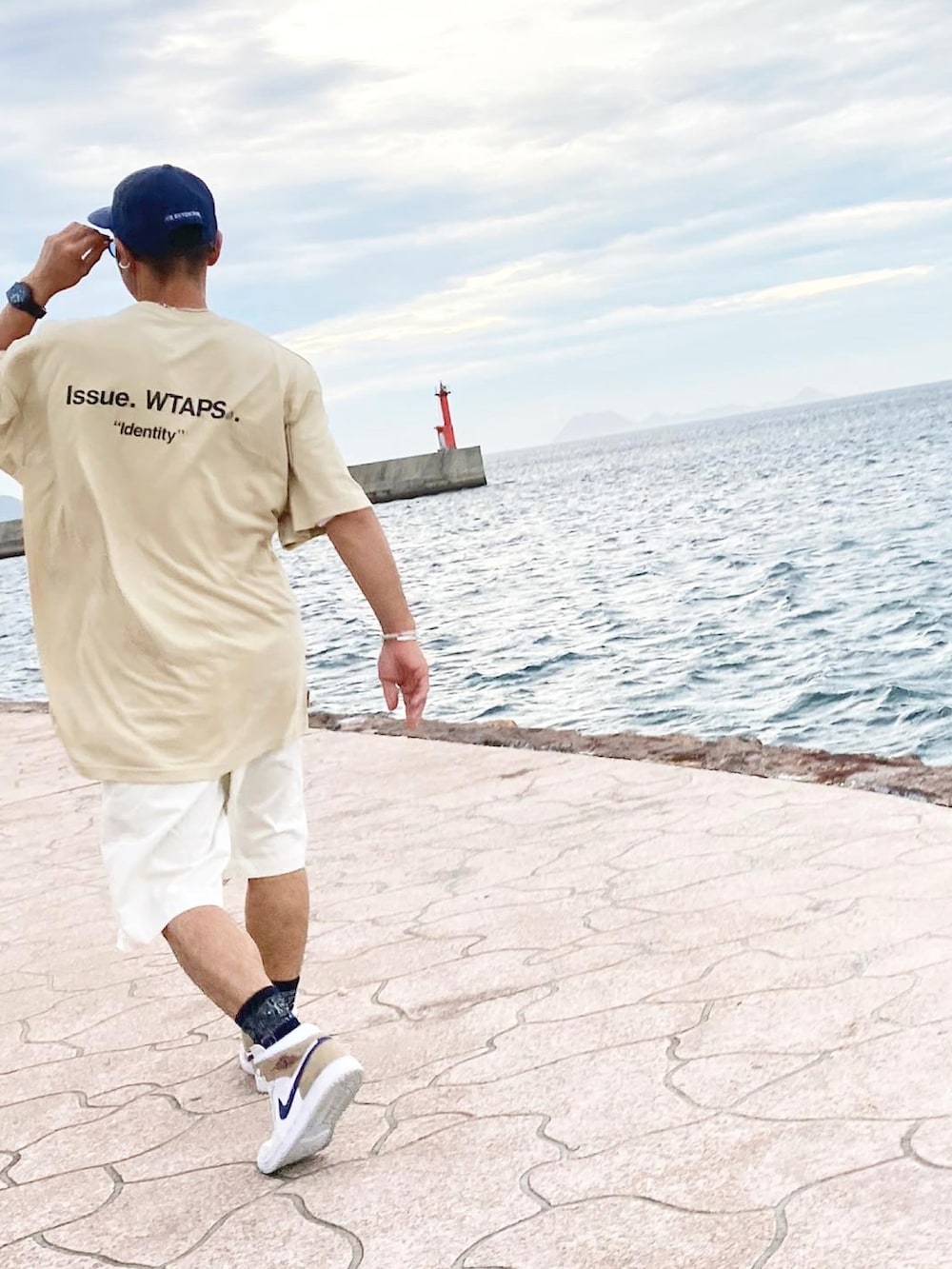 ベージュ系のTシャツ/カットソー、ホワイト系のチノパンツ、ベージュ系のスニーカーを着用したメンズの夏コーディネートの2枚目の写真