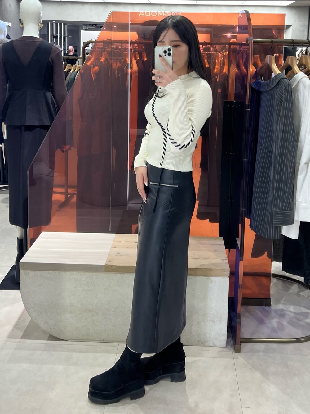 ブラック系のスカート、ホワイト系のニット/セーター、ブラック系のブーツを着用したレディースの秋コーディネートの2枚目の写真