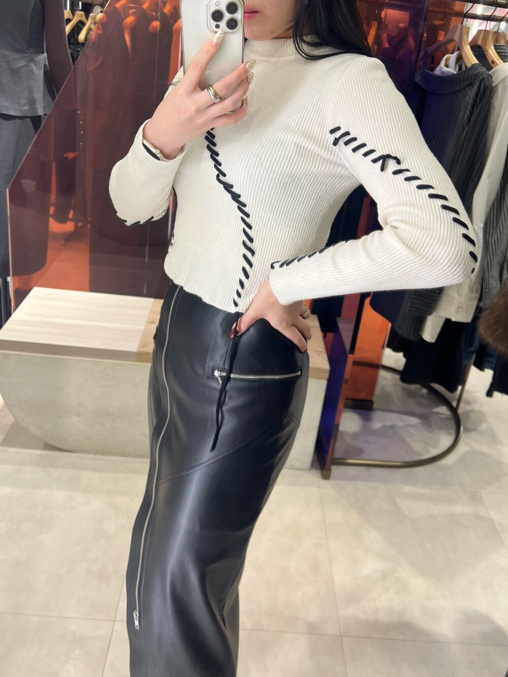 ブラック系のスカート、ホワイト系のニット/セーター、ブラック系のブーツを着用したレディースの秋コーディネートの3枚目の写真