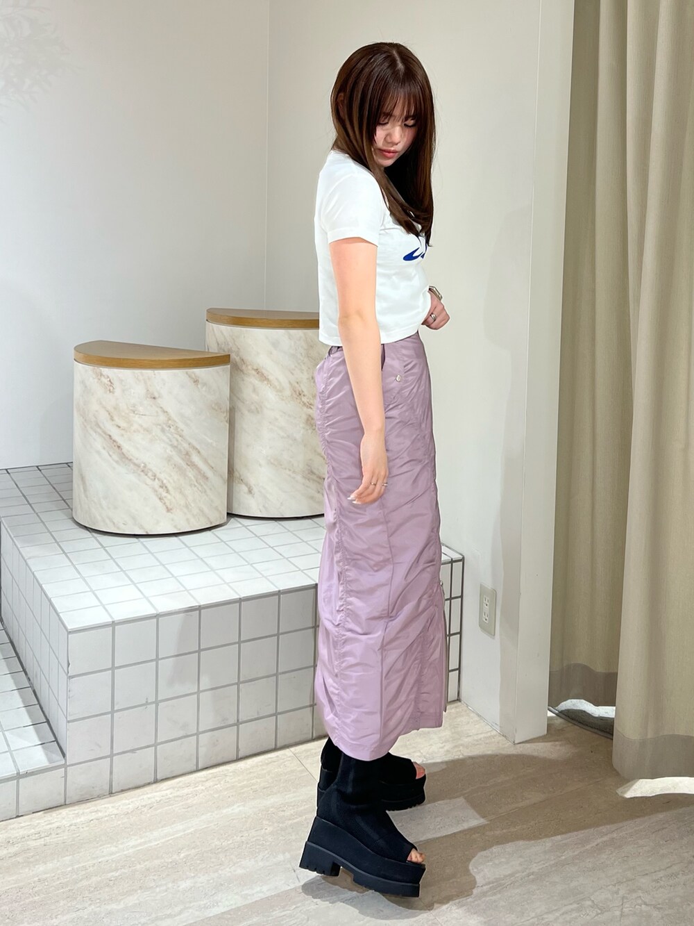 ピンク系のスカート、ホワイト系のTシャツ/カットソー、ブラック系のサンダルを着用したレディースの春コーディネートの2枚目の写真