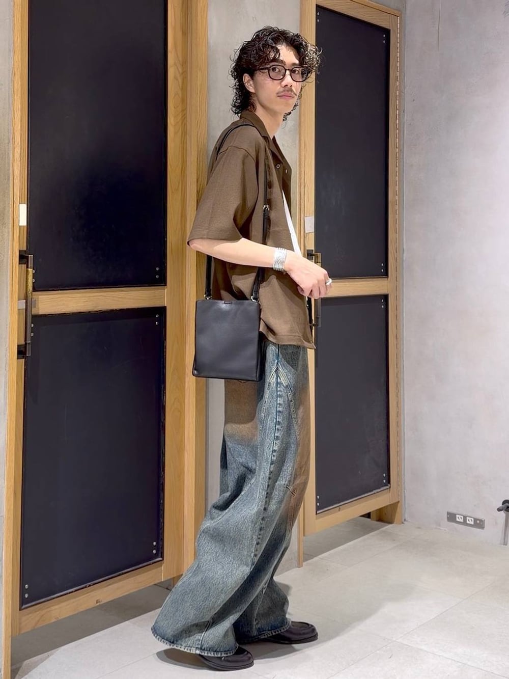 ブラック系のショルダーバッグ、ブラウン系のシャツ/ブラウス、ブラック系のローファーを着用したメンズの夏コーディネートの3枚目の写真