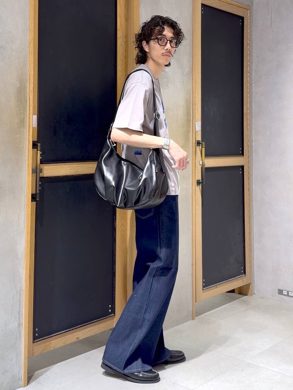 ブラック系のショルダーバッグ、ブラック系のモカシン/デッキシューズ、ブルー系のデニムパンツを着用したメンズの夏コーディネートの3枚目の写真