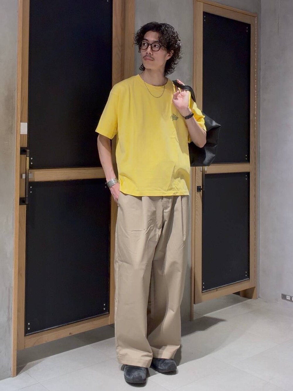 ブラック系のショルダーバッグ、ベージュ系のチノパンツ、イエロー系のTシャツ/カットソーを着用したメンズの春コーディネートの3枚目の写真