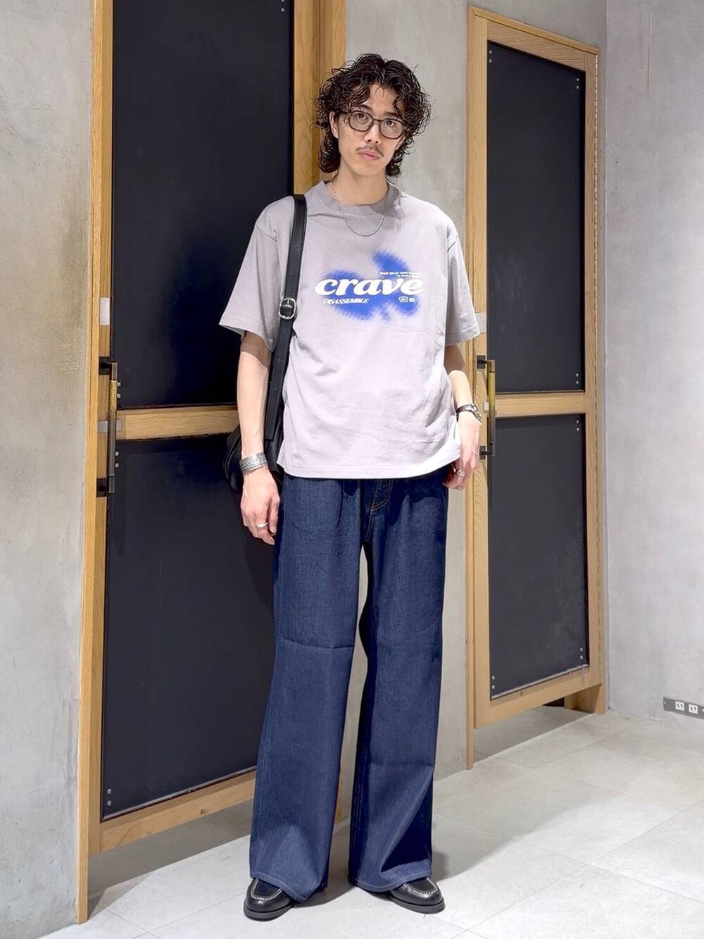 ブラック系のショルダーバッグ、ブラック系のモカシン/デッキシューズ、ブルー系のデニムパンツを着用したメンズの夏コーディネートの4枚目の写真