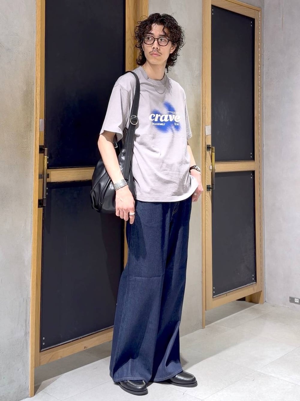 ブラック系のショルダーバッグ、ブラック系のモカシン/デッキシューズ、ブルー系のデニムパンツを着用したメンズの夏コーディネートの2枚目の写真