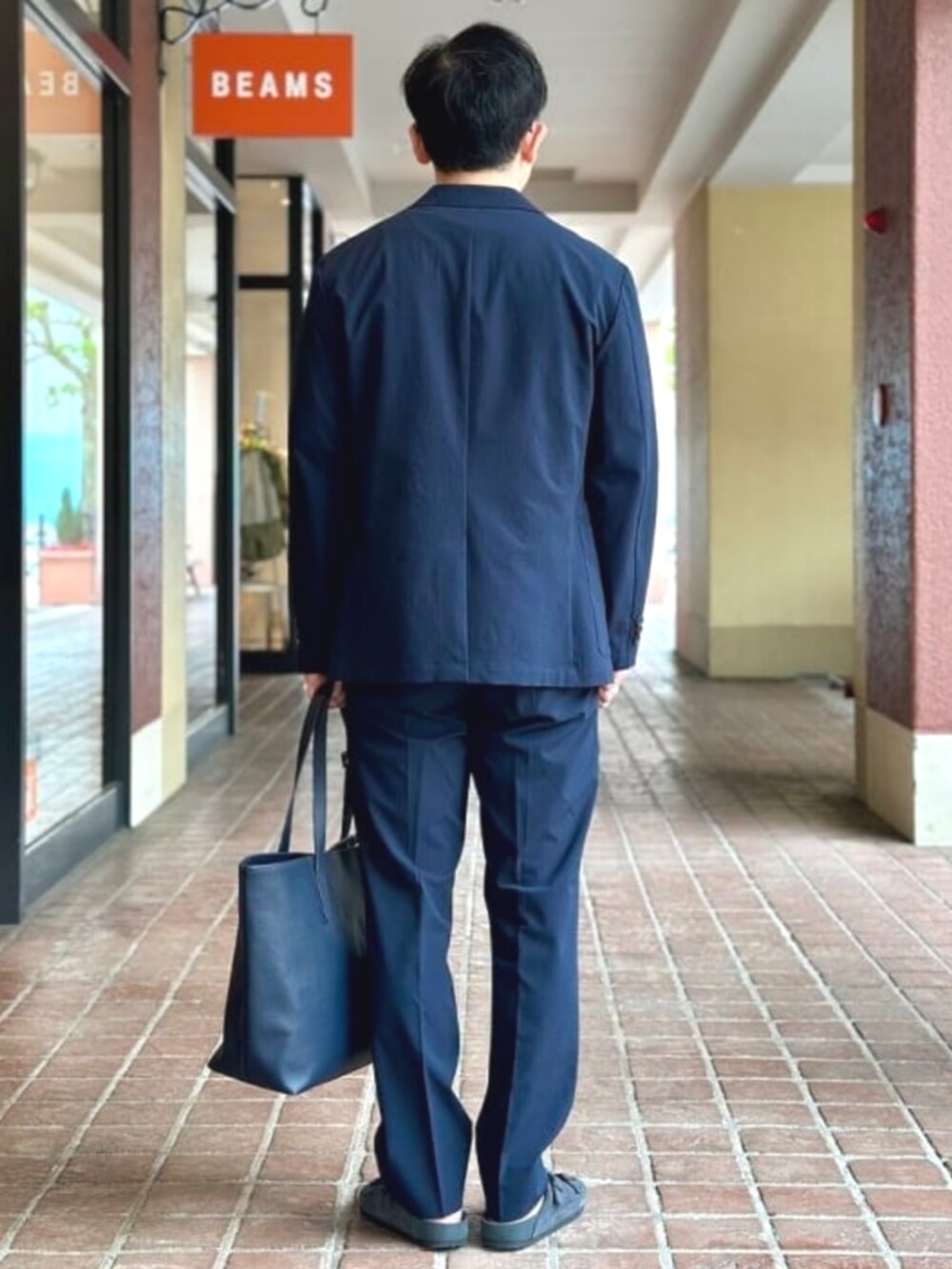 ブルー系のトートバッグ、ベージュ系のTシャツ/カットソー、ブルー系のテーラードジャケットを着用したメンズの夏コーディネートの3枚目の写真