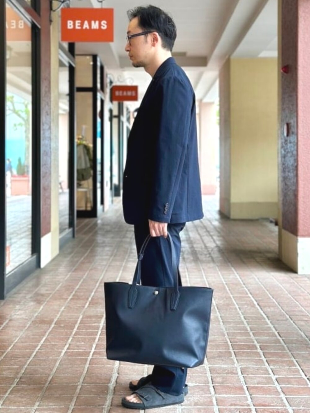 ブルー系のトートバッグ、ベージュ系のTシャツ/カットソー、ブルー系のテーラードジャケットを着用したメンズの夏コーディネートの2枚目の写真