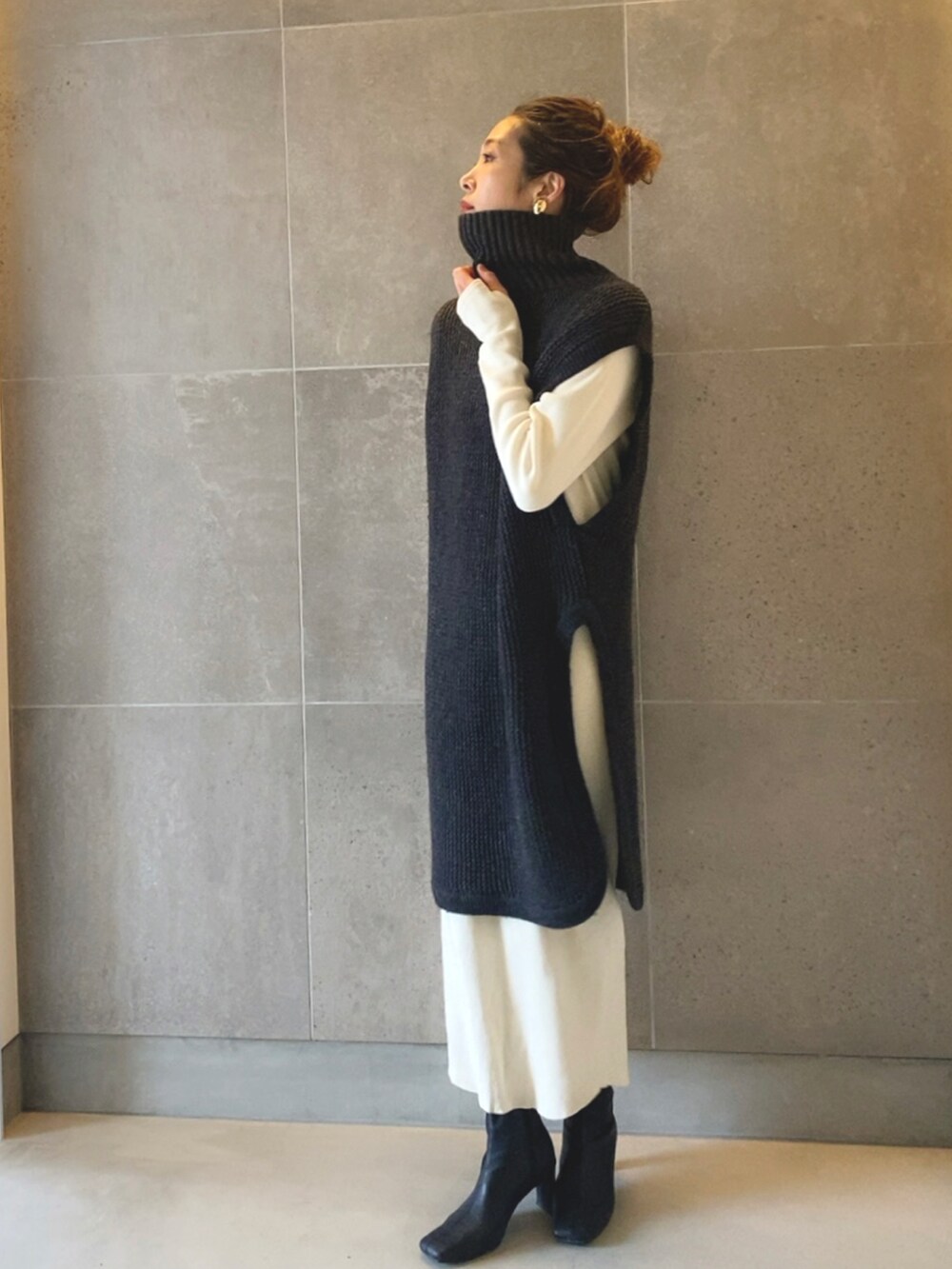 グレー系のベスト、ホワイト系のワンピース、ブラック系のブーツを着用したレディースの春コーディネートの2枚目の写真