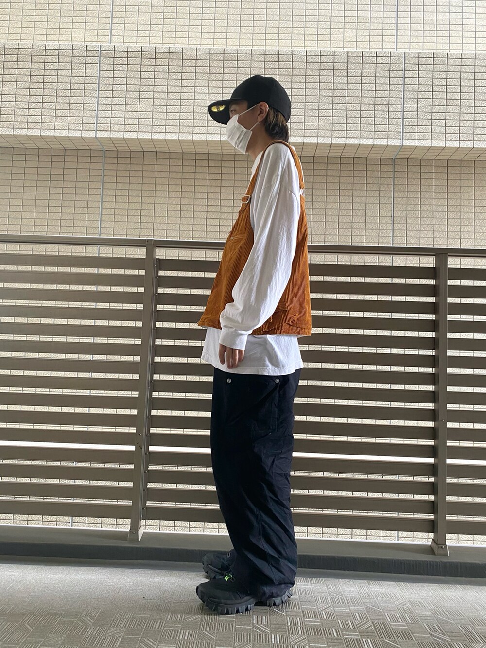 オレンジ系のベスト、ブラック系のカーゴパンツ、ブラック系のスニーカーを着用したメンズの春コーディネートの2枚目の写真