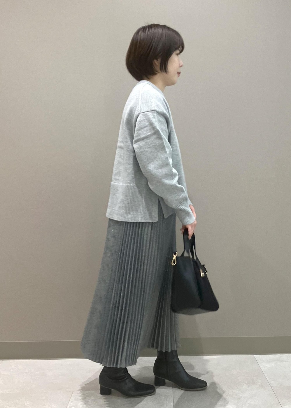 グレー系のニット/セーター、ブラック系のブーツ、ブラック系のトートバッグを着用したレディースの秋コーディネートの2枚目の写真