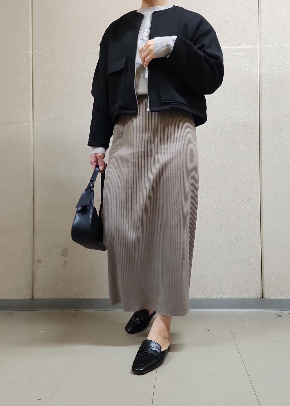 ブラック系のハンドバッグ、ブラウン系のスカート、グレー系のニット/セーターを着用したレディースの春コーディネートの2枚目の写真