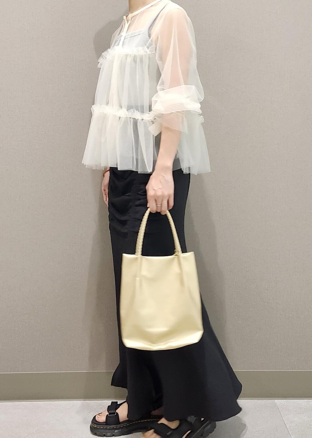 グレー系のタンクトップ、ホワイト系のカーディガン/ボレロ、ゴールド系のトートバッグを着用したレディースの夏コーディネートの2枚目の写真