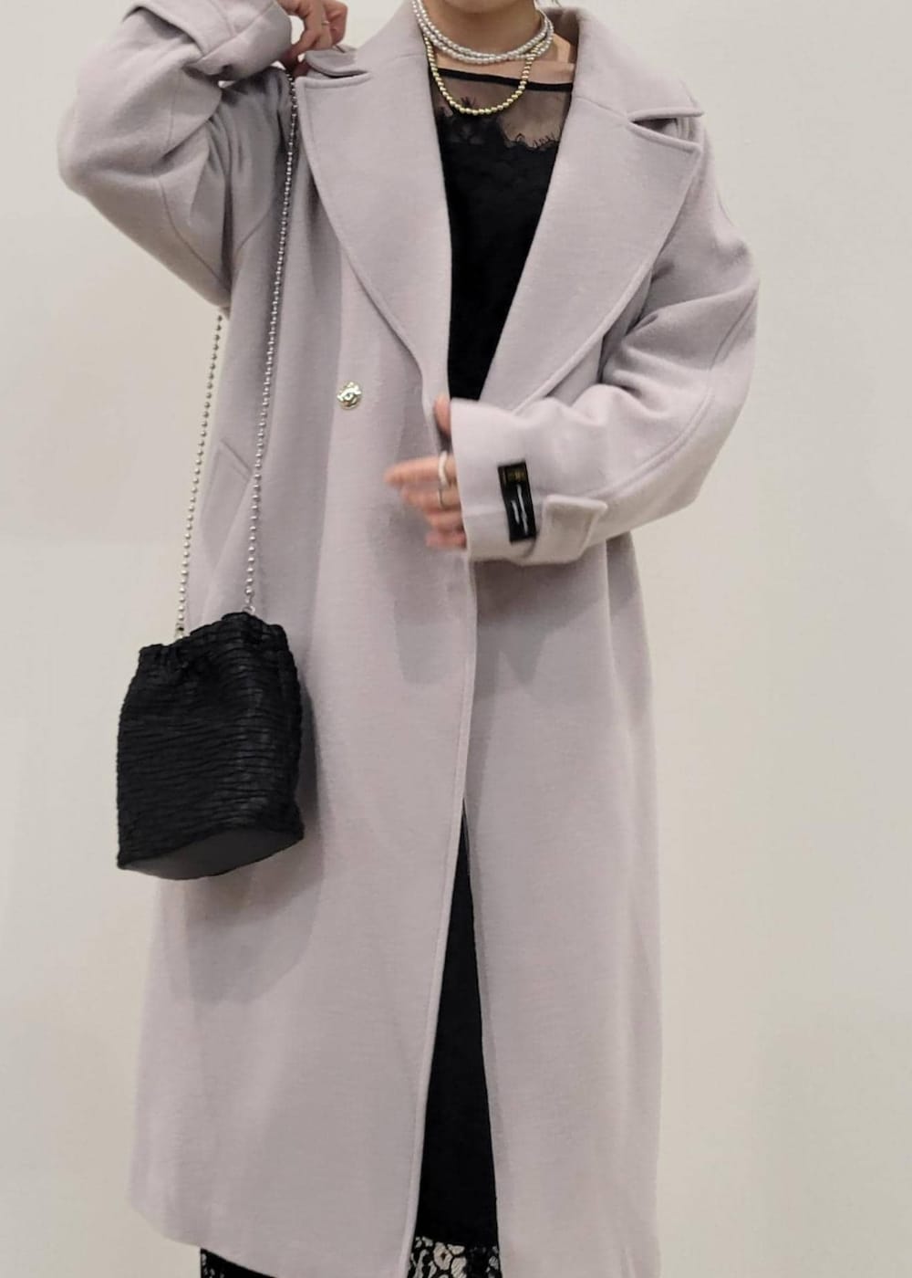 ベージュ系のパンプス、グレー系のチェスターコート、ブラック系のドレスを着用したレディースの冬コーディネートの3枚目の写真