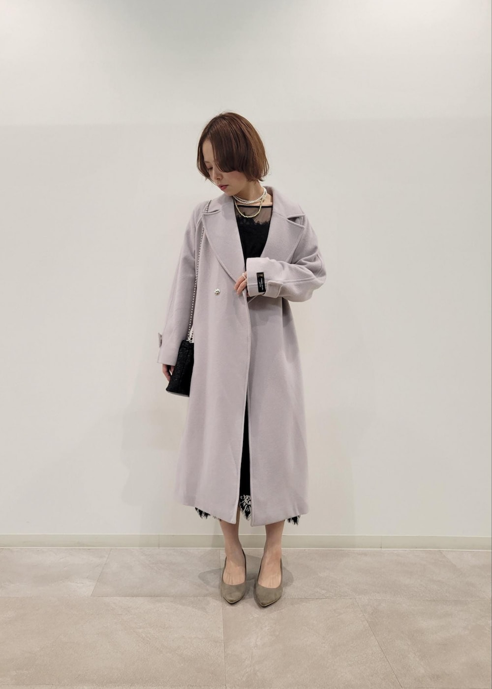 ベージュ系のパンプス、グレー系のチェスターコート、ブラック系のドレスを着用したレディースの冬コーディネートの2枚目の写真