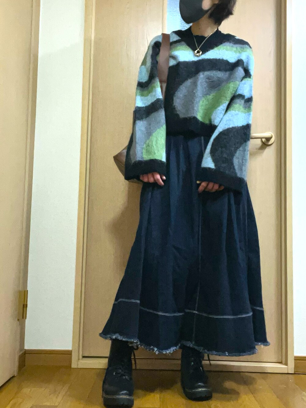 ブルー系のデニムスカート、ブラック系のブーツ、グリーン系のニット/セーターを着用したレディースの春コーディネートの2枚目の写真