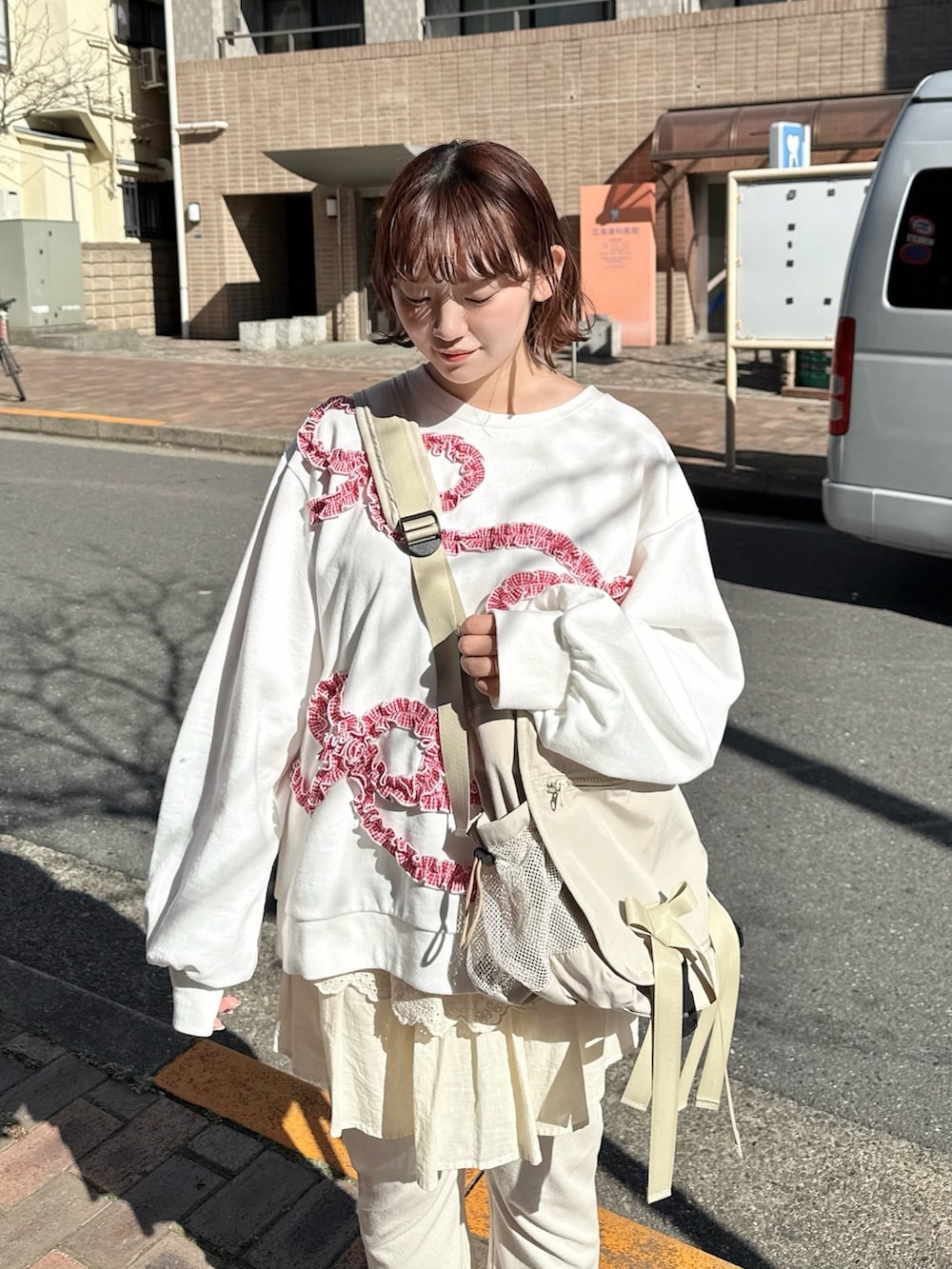 ホワイト系のスウェット、ベージュ系のメッセンジャーバッグ、ホワイト系のスウェットパンツを着用したレディースの冬コーディネートの3枚目の写真