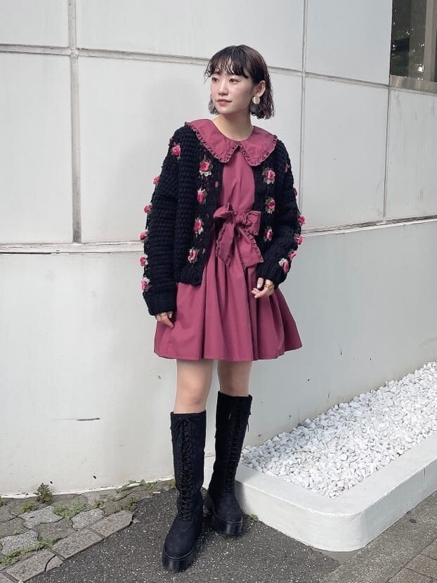 レッド系のワンピース、ブラック系のカーディガン/ボレロ、ブラック系のブーツを着用したレディースの秋コーディネートの2枚目の写真