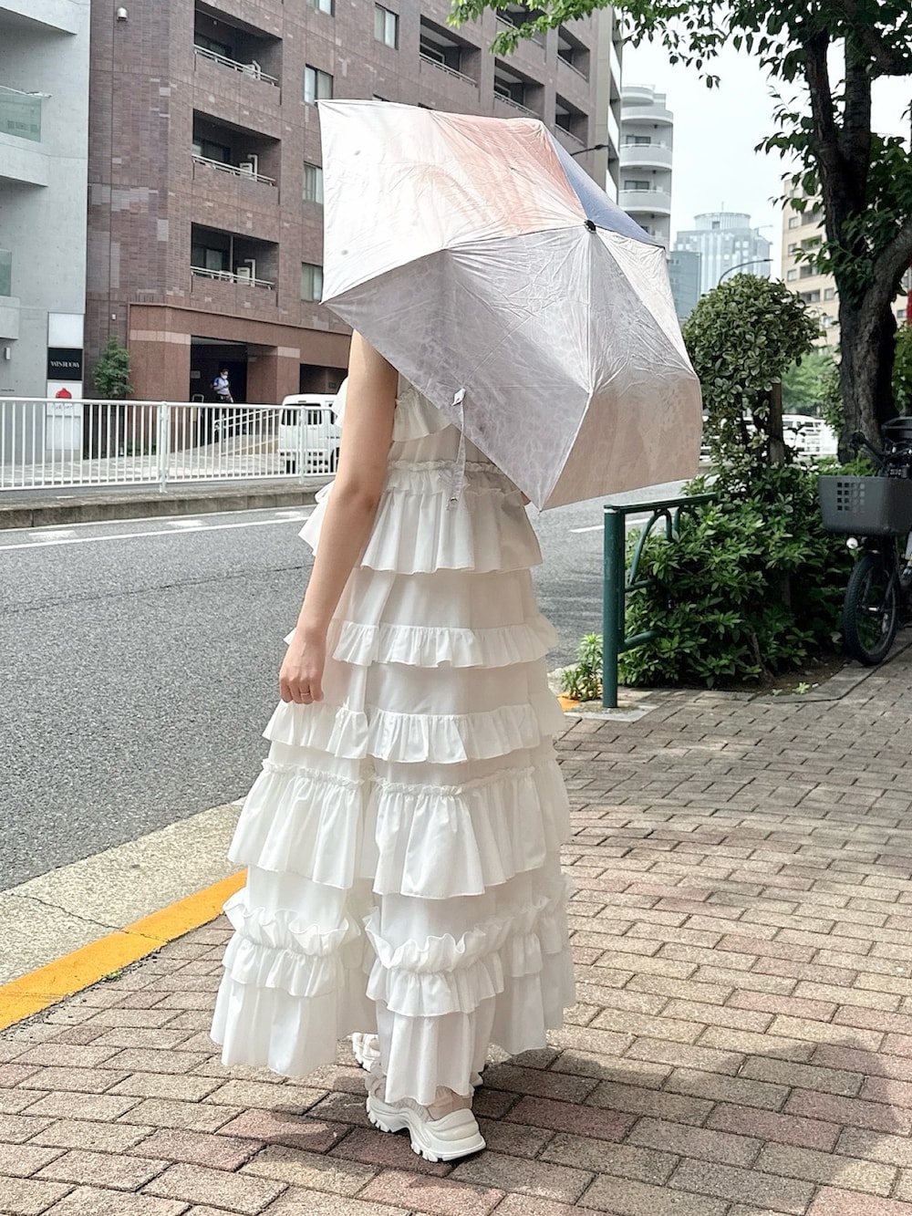 ホワイト系のワンピース、ピンク系のスニーカー、ピンク系の長傘を着用したレディースの春コーディネートの2枚目の写真