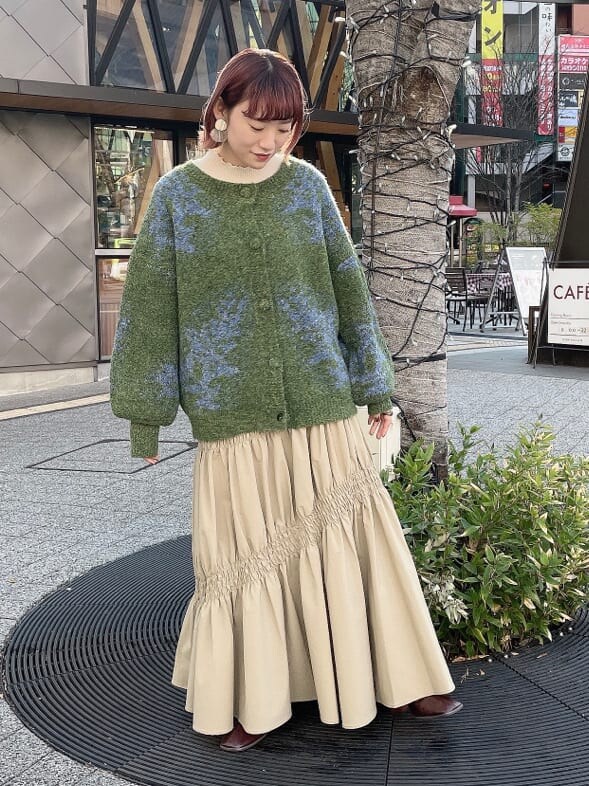 グリーン系のカーディガン/ボレロ、ベージュ系のスカート、ホワイト系のニット/セーターを着用したレディースの冬コーディネートの2枚目の写真