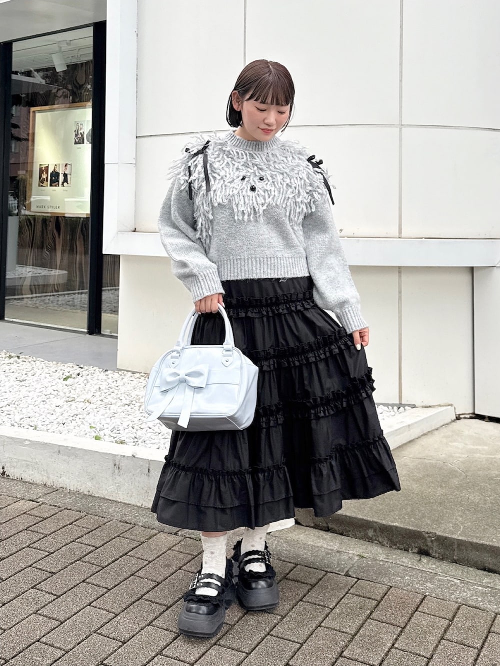 グレー系のニット/セーター、ブラック系のスカート、ブラック系のスニーカーを着用したレディースの夏コーディネートの2枚目の写真
