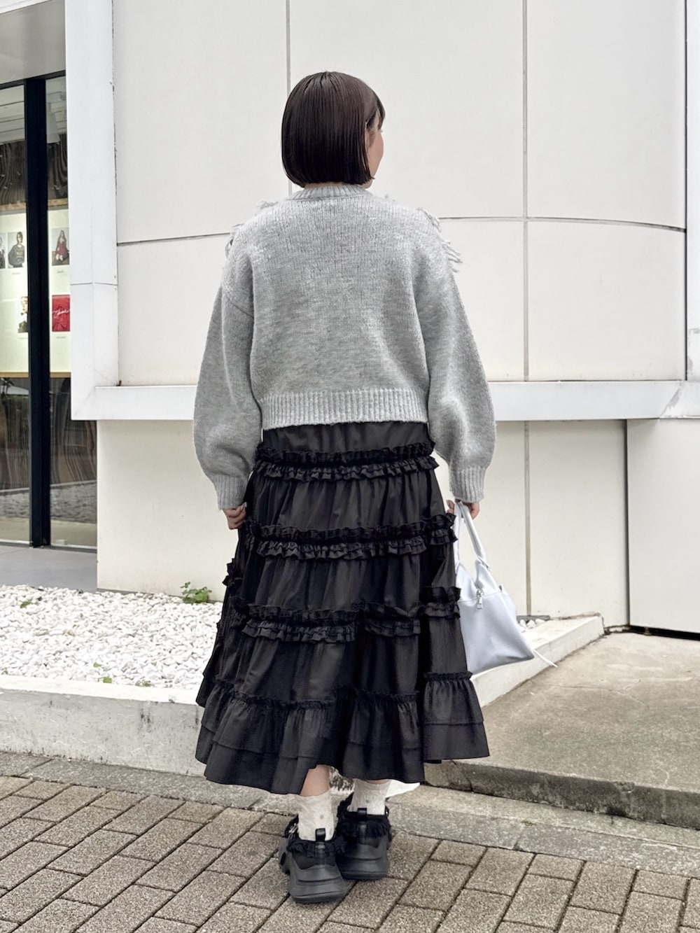 グレー系のニット/セーター、ブラック系のスカート、ブラック系のスニーカーを着用したレディースの夏コーディネートの3枚目の写真