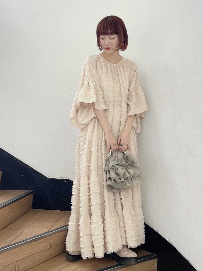 ベージュ系のドレス、グリーン系のハンドバッグ、ベージュ系のブーツを着用したレディースの夏コーディネートの2枚目の写真